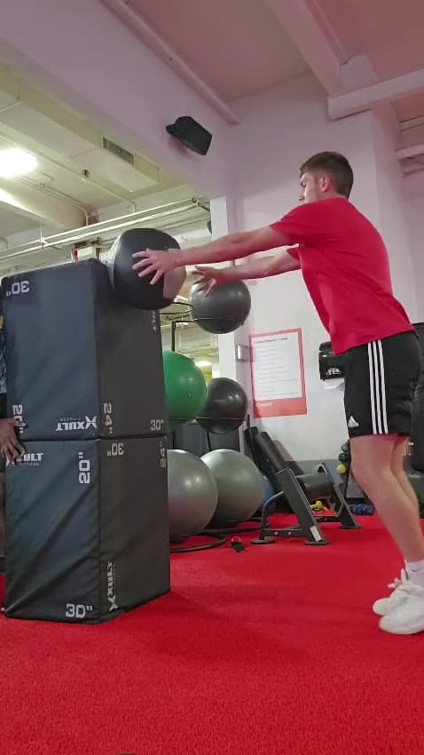 A client throwing a medicine ball against a plyo box