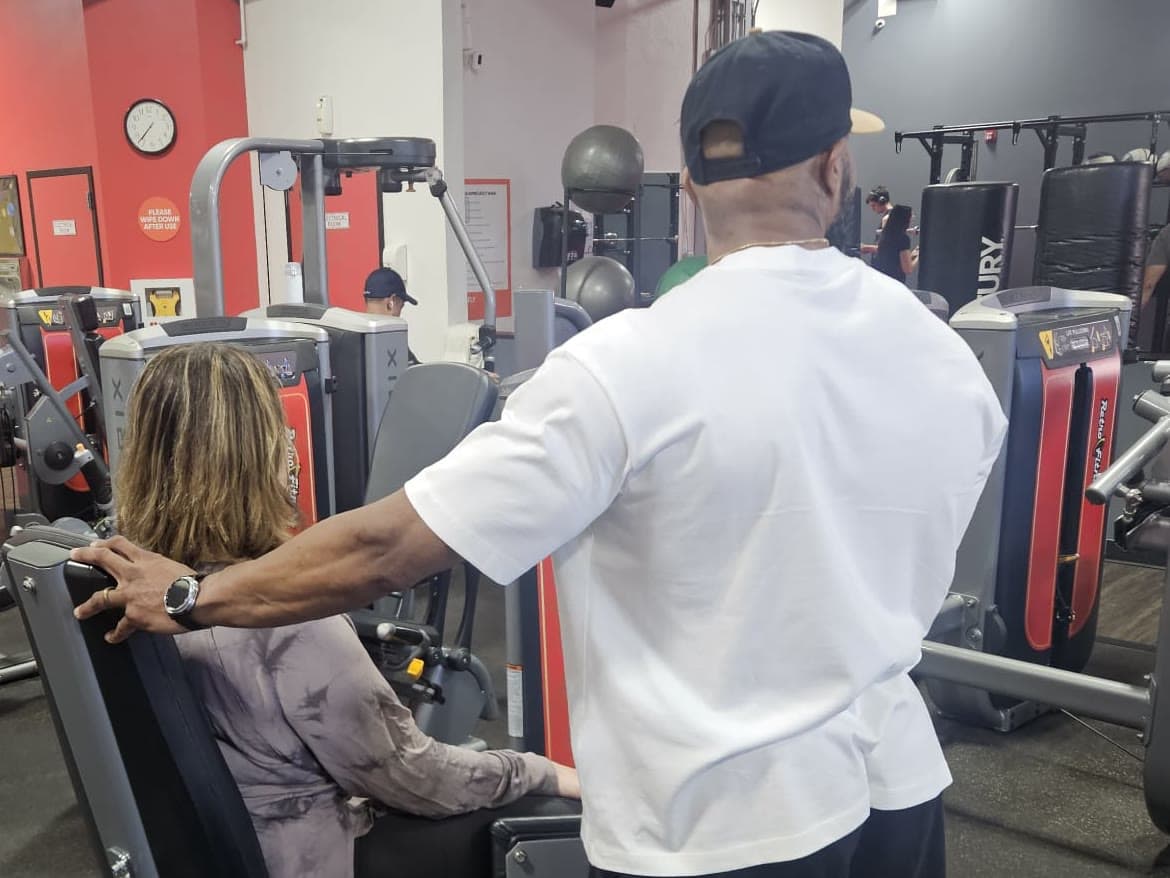 Daine Chang standing beside a client seated on a machine, guiding the movement