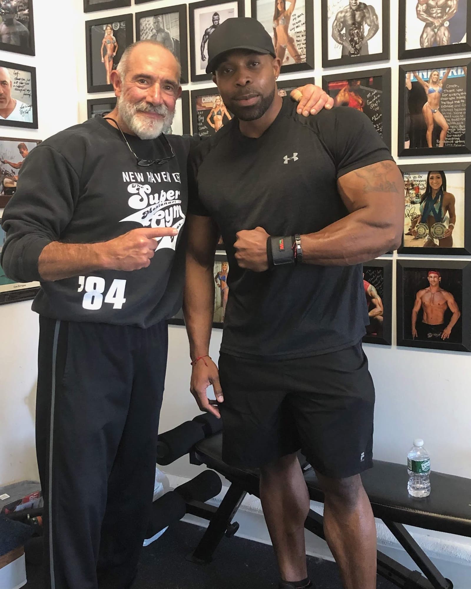 Daine Chang with a bodybuilder in front of a wall of contest photos